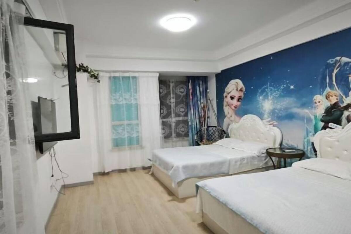 A hotel room with two beds, a large mural of animated characters, a mirror, and a small round table.