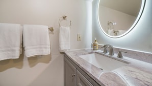 Une salle de bain avec un lavabo en marbre, un grand miroir et deux serviettes suspendues à des crochets.