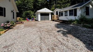 Une allée de gravier mène à une maison avec un garage et un petit abri de jardin.