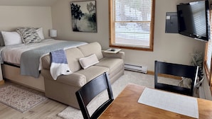 Une chambre à coucher avec un lit, un canapé, une télévision et une fenêtre avec des stores.