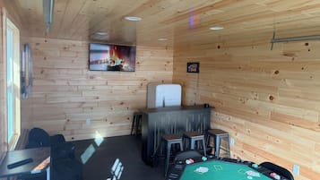 Un intérieur en bois avec une table de billard, un coin bar et un téléviseur diffusant une image de feu de cheminée.