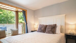 Ein Schlafzimmer mit einem großen Bett, einem hölzernen Kopfteil, zwei Nachttischlampen und Blick durch ein Fenster mit einem Holzbalkon.