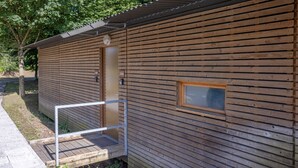 Una cabaña de madera con una puerta, un ventanal pequeño y una barandilla metálica.