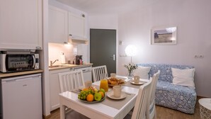 Cocina compacta con microondas, lavaplatos y refrigerador pequeño. Una mesa de comedor con frutero y cafetera.