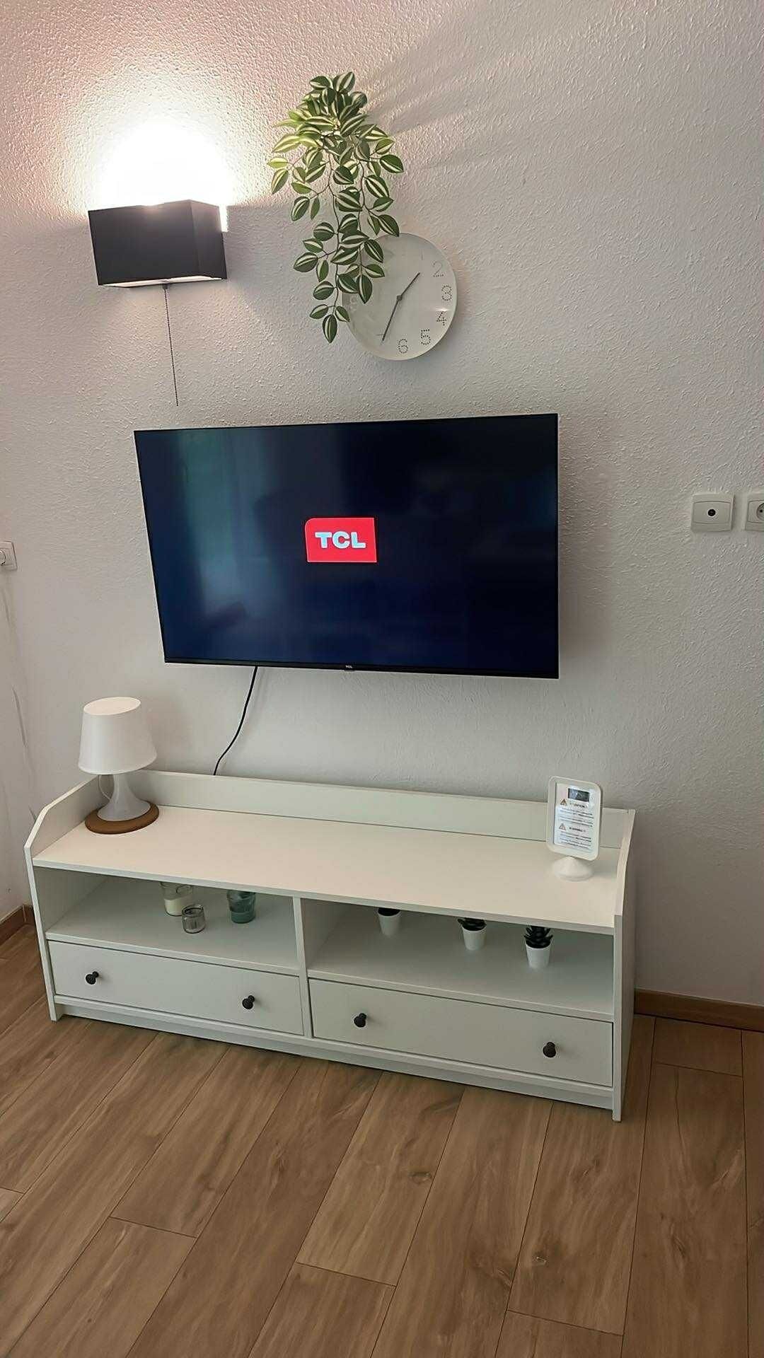 En platt-TV som är monterad på en vägg ovanför ett vitt TV-bord med lådor.