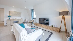 A modern living room with a sofa, TV, and a floor lamp. - Le Vertigo - Appt proche de la plage (Dinard)