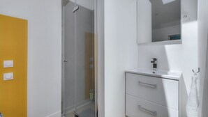 A bathroom with a glass shower enclosure, a white vanity with a mirror, and a yellow wall. - L'Ormeau - Charmant appt (Toulouse)