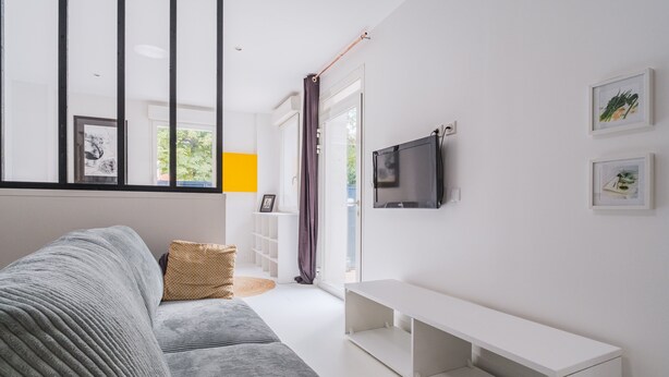 Una sala de estar moderna con un sofá gris, un banco blanco, un televisor de pantalla plana y cuadros en la pared.