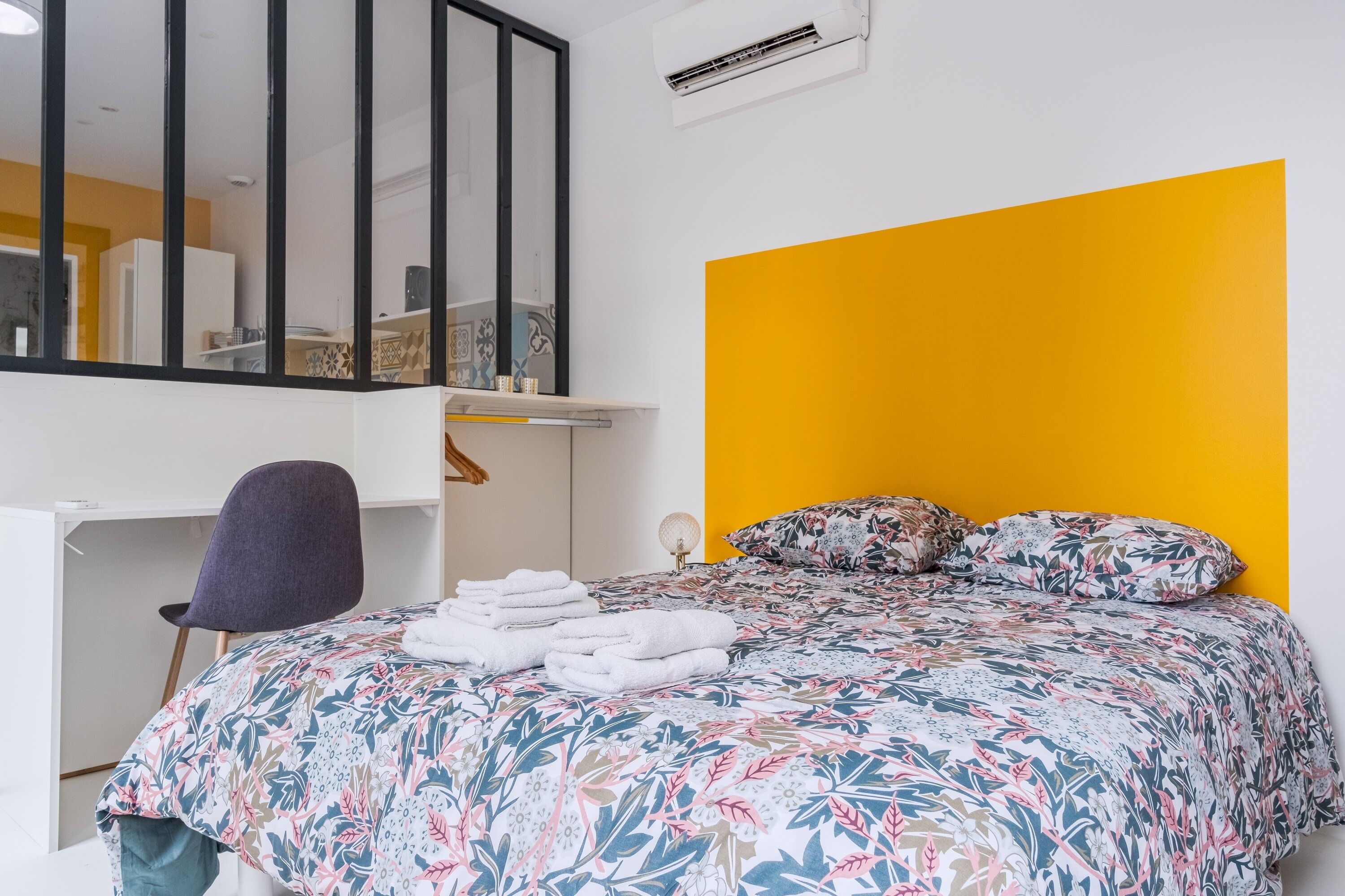 A bedroom with a bed, a desk, a chair, and a mirror.