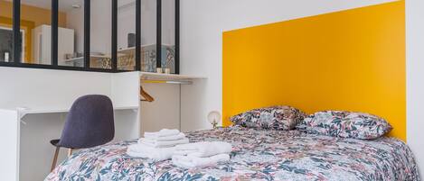 A bedroom with a bed, a desk, a chair, and a mirror.