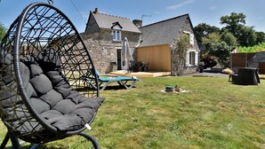 A stone house with a patio, a hanging chair, and a wooden deck.