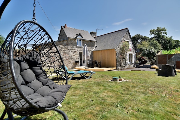 Relax in a serene backyard with a hanging chair, wooden deck, and traditional house.