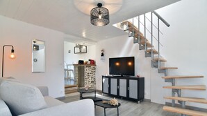 A modern living room with a grey sofa, a black entertainment unit, a TV, and a staircase with wooden steps.