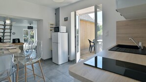 A modern kitchen with a built-in stove, a microwave, and a refrigerator. There are clear plastic chairs and a dining table.