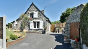 A stone house with a paved driveway, wooden gate, and potted plants.
