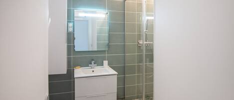 A bathroom with a white sink, mirror, and cabinet, and a glass shower enclosure.