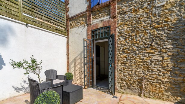 An outdoor patio with wicker furniture, a potted plant, and a stone wall. - Cozy Corner - Appt avec jardin pour 4 (Tournan-en-Brie)