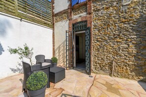 An outdoor patio with wicker furniture, a potted plant, and a stone wall. - Cozy Corner - Appt avec jardin pour 4 (Tournan-en-Brie)