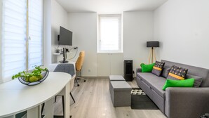 A modern living room with a grey sofa, a white table, a black TV, a grey office chair, and a small plant on the table. - Cozy Corner - Appt avec jardin pour 4 (Tournan-en-Brie)