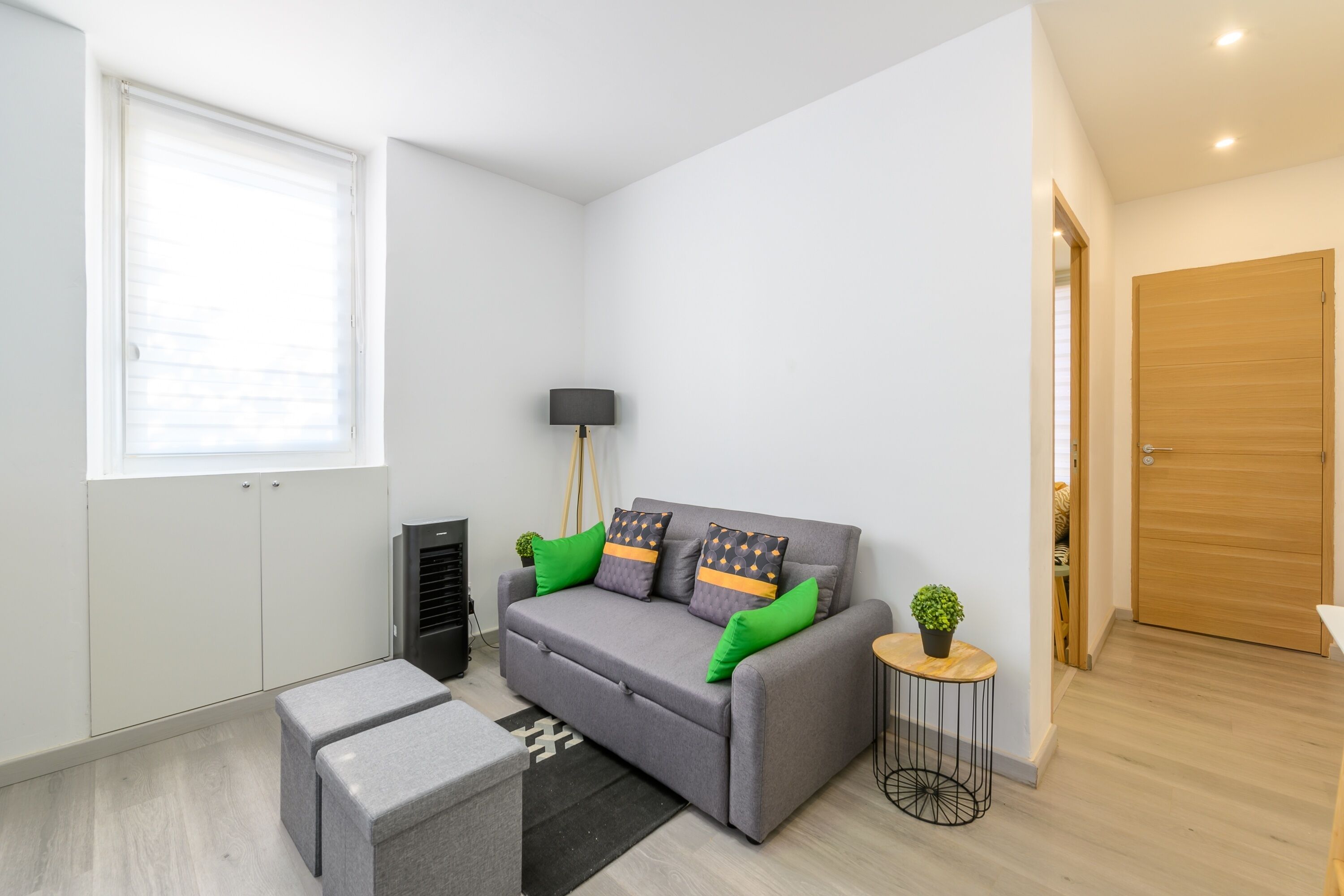 Una sala de estar moderna con un sofá gris, una mesita redonda con una planta, una lámpara de pie negra y un otoman gris.