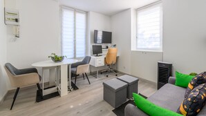 A modern, well-lit room with a dining table, two chairs, a sofa with cushions, a TV, and a small desk with a computer. - Cozy Corner - Appt avec jardin pour 4 (Tournan-en-Brie)
