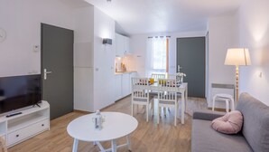 Ein modernes Wohnzimmer mit Flachbildfernseher, rundem Couchtisch, einer Couch und einem Essbereich mit Tisch und Stühlen.