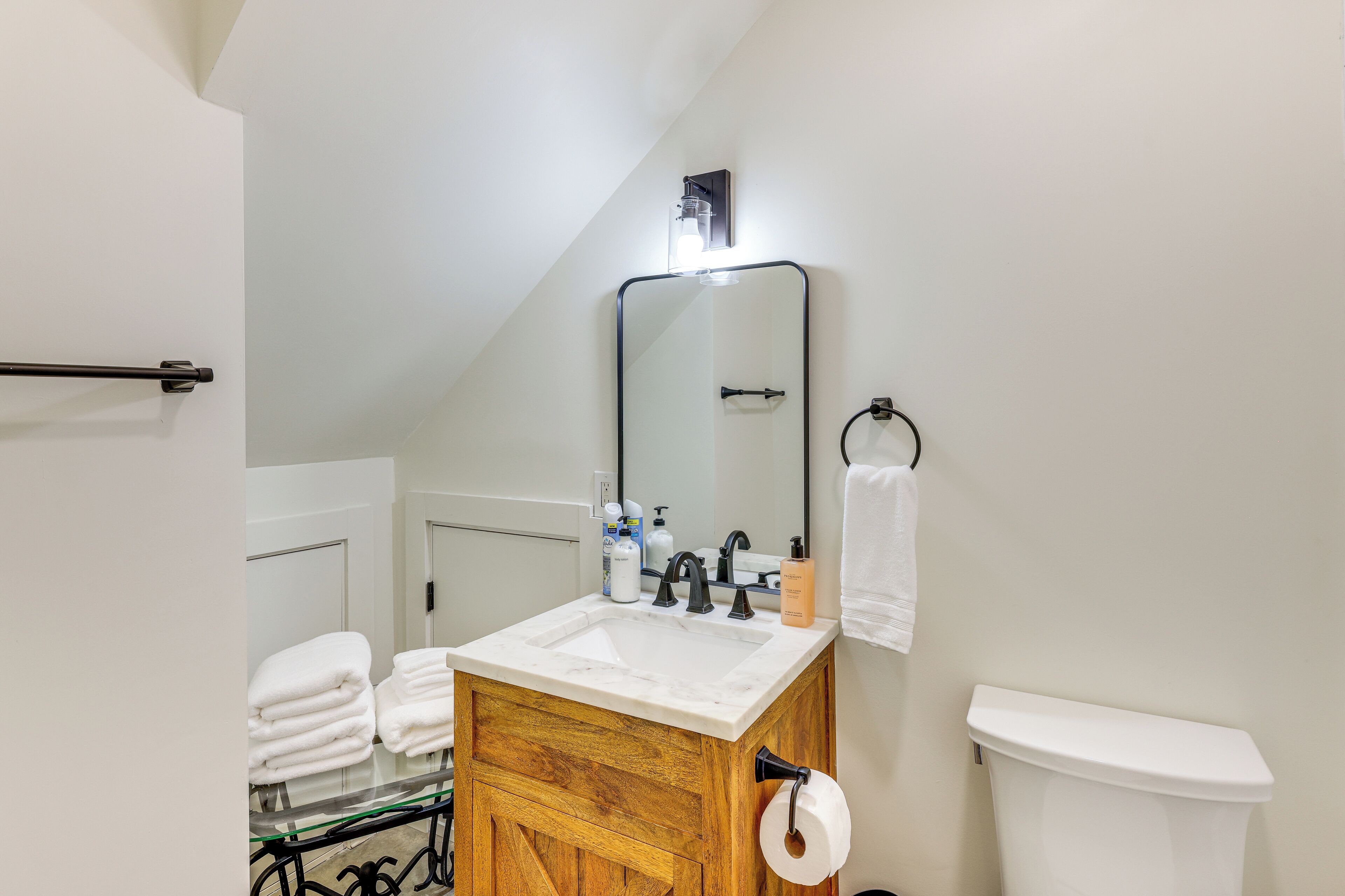 A bathroom with a white sink, wooden vanity, a mirror, a towel rack, and a toilet.