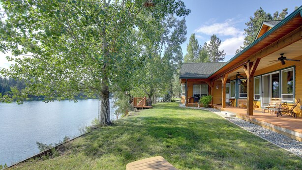 A lakeside cabin with a deck, outdoor seating, and a view of the lake. - Clark Fork Riverfront Home w/ Dock! (Thompson Falls)