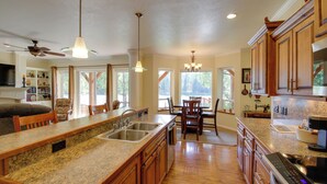 A spacious kitchen with granite countertops, wooden cabinets, and a large island with a sink. There is a dining area with a table and chairs, and a ceiling fan. - Clark Fork Riverfront Home w/ Dock! (Thompson Falls)
