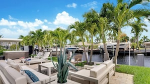 A waterfront patio with outdoor seating, palm trees, and boats in the background.