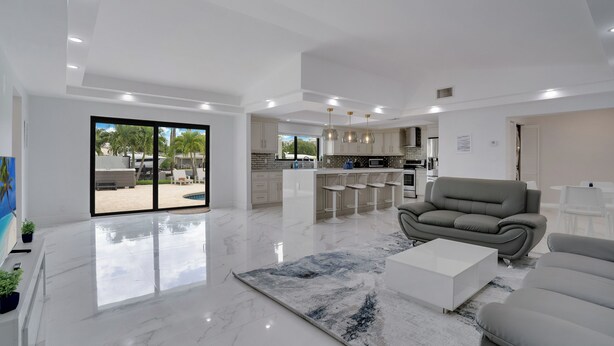 A spacious living area with a large window, a kitchen with bar stools, and a grey sofa.