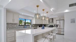 A modern kitchen with white cabinetry, a large island with bar stools, and pendant lighting.