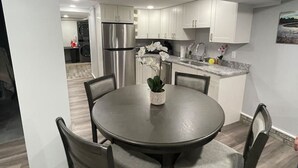 A modern kitchen with white cabinets, stainless steel appliances, and a dining area with a round table and chairs. - Downtown TC Two Unit Retreat on the Water - Sleeps 10 (Traverse City)