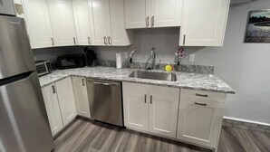 A modern kitchen with white cabinets, a stainless steel refrigerator, a microwave, and a dishwasher. - Downtown TC Two Unit Retreat on the Water - Sleeps 10 (Traverse City)