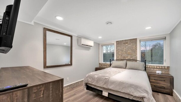 A bedroom with a bed, bedside tables, a dresser, a TV, and a window with a view. - Downtown TC Two Unit Retreat on the Water - Sleeps 10 (Traverse City)