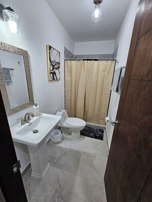 Une salle de bain avec un lavabo blanc, des toilettes et un rideau de douche.