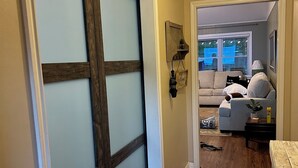 Un pasillo con puerta corredera, suelo de madera, sofá y una mesa con lámpara.