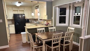Una cocina con armarios blancos, un refrigerador negro, una encimera de granito y una mesa de comedor con sillas.