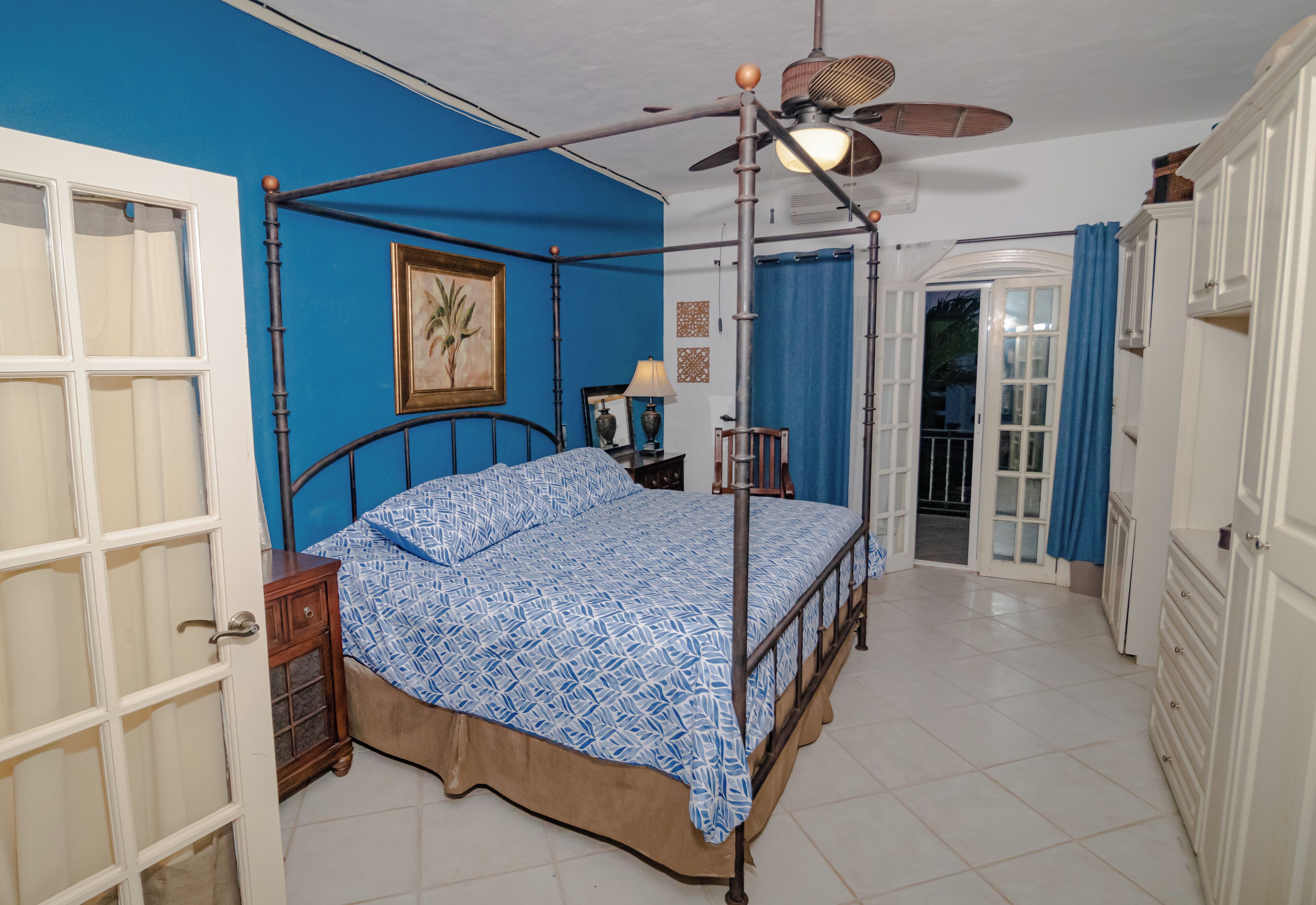 Ein Schlafzimmer mit Himmelbett, Deckenventilator und einer Tür zu einem Außenbereich.