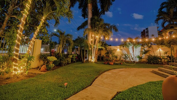 A well-lit garden with palm trees, a concrete pathway, and string lights. - Villas Mi Mexico (Bucerías)