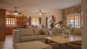 A spacious living room with a sectional sofa, a coffee table, and a dining area with wooden cabinets and a chandelier. - Villas Mi Mexico (Bucerías)