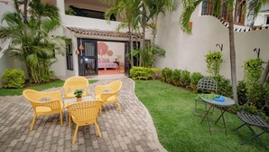 A courtyard with a patio area featuring yellow wicker chairs, a small table, and a metal table with a blue cushion. - Villas Mi Mexico (Bucerías)
