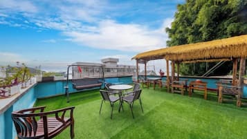Una terraza en la azotea con piscina, mobiliario exterior y una estructura de techo de paja.