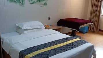 A neatly made bed with a white and blue bedspread, a wooden nightstand with a red cloth, and a wall with a green landscape painting.