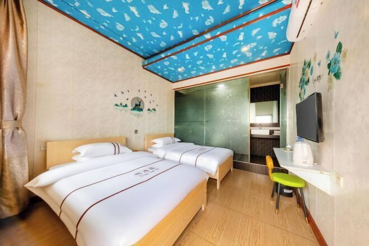 A hotel room with a bed, two bedside tables, a chair, a TV, and a bathroom visible through an open door.