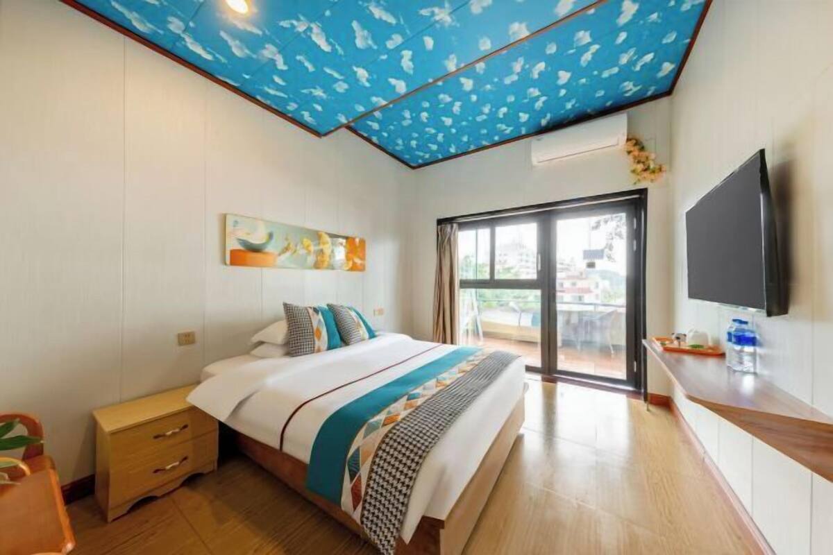 A hotel room with a bed, a nightstand, a TV, and a view of the outdoors.