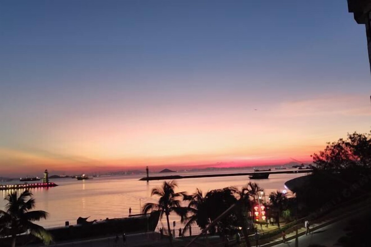A sunset view over a calm body of water with a bridge and distant landmass.