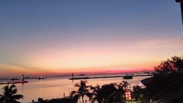 A sunset view over a calm body of water with a bridge and distant landmass.