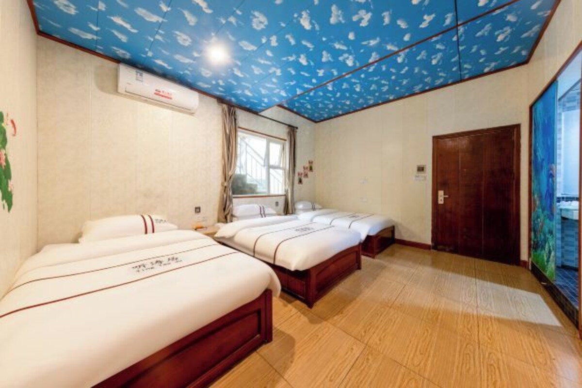 A hotel room with three beds, a ceiling with a fish pattern, an air conditioning unit, a window with curtains, and a wooden door.