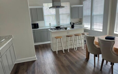 A modern kitchen with grey cabinets, a central island with stools, and a dining area with a table and chairs.